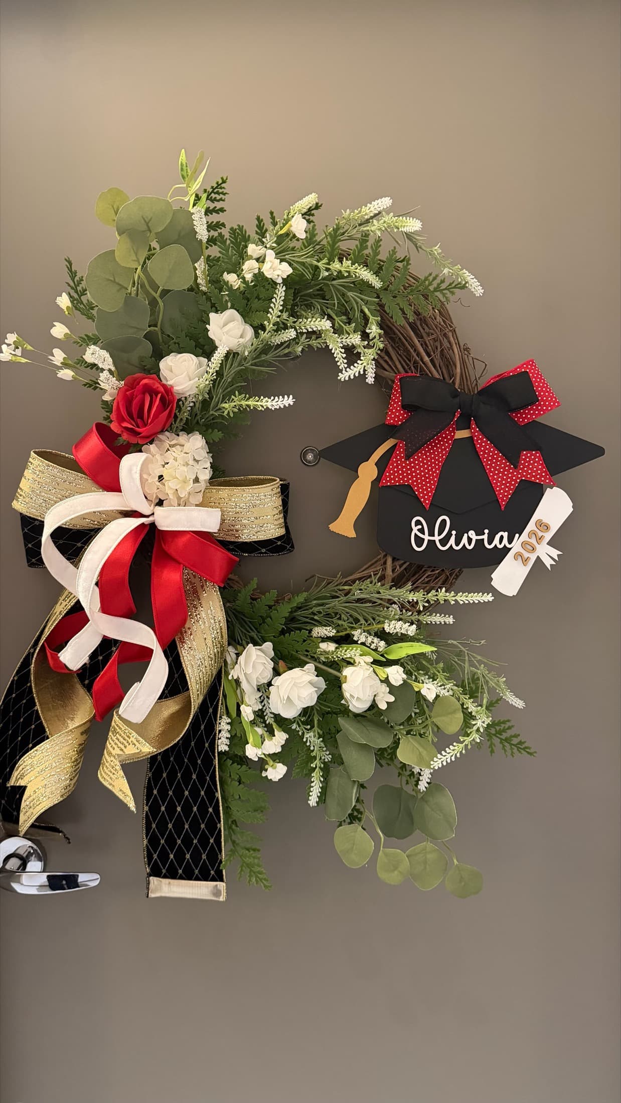 Greenery door swag with red roses, white accents, ribbon, and a small name tag.