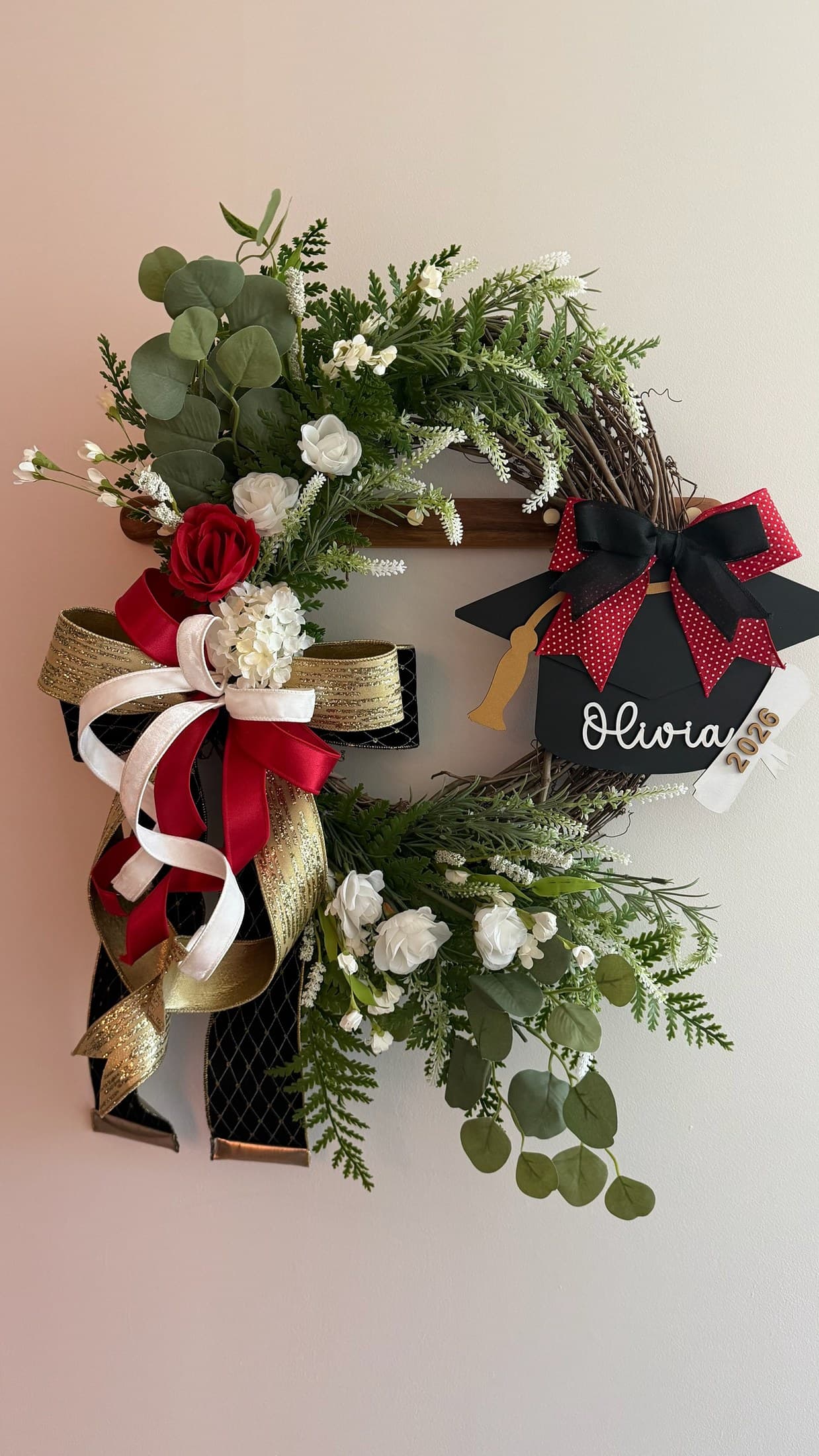 Wall-mounted greenery swag with red roses, white accents, and trailing ribbon.