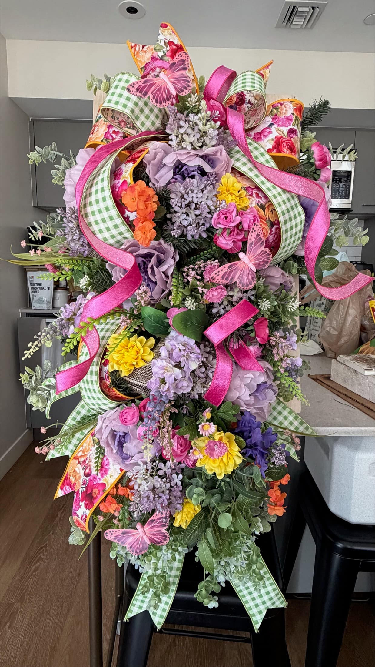 Colorful floral door swag with pink ribbon, greenery, and spring accents.
