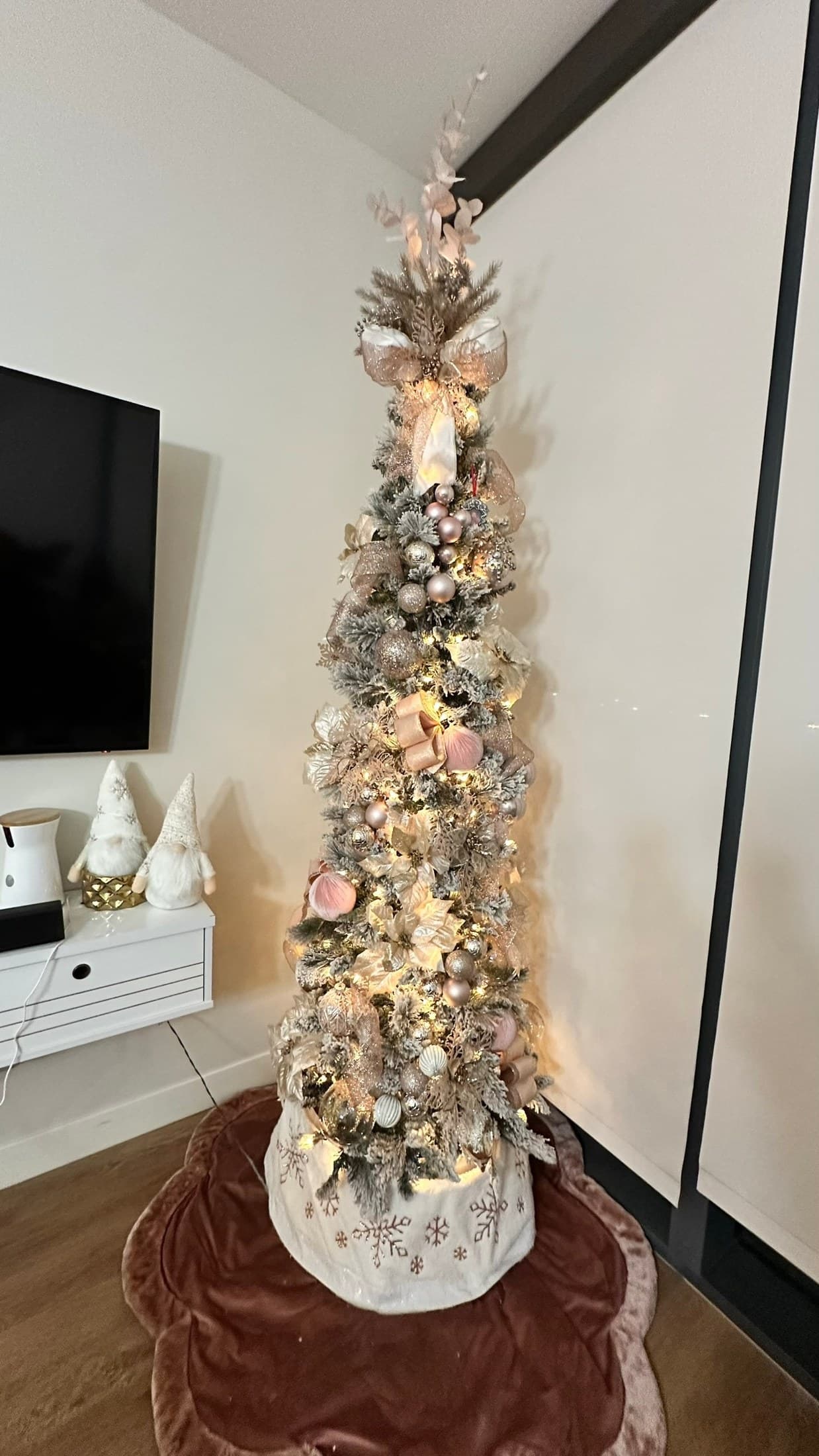 Warm pencil Christmas tree with ribbon styled beside a console in a cozy living room.